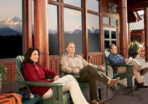 Guests sitting on deck with Denali in window reflection at Mt. McKinley Princess Wilderness Lodge, Alaska